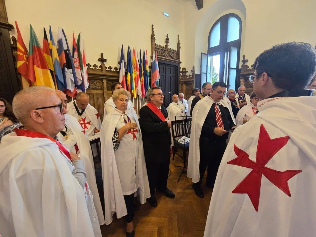 Cérémonie en salle, avec des membres en manteaux blancs à croix rouge et des drapeaux internationaux